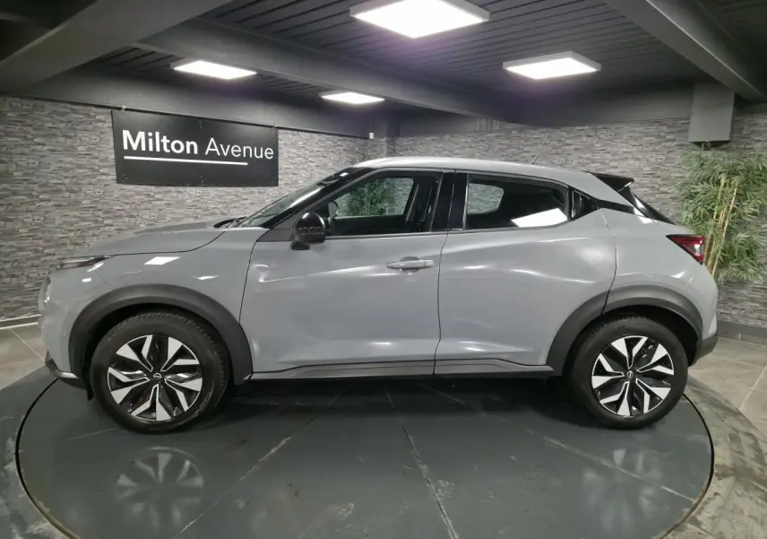 Vue de profil côté gauche d'un Nissan Juke gris métallisé 2023 avec jantes bi-ton et rétroviseurs noirs.