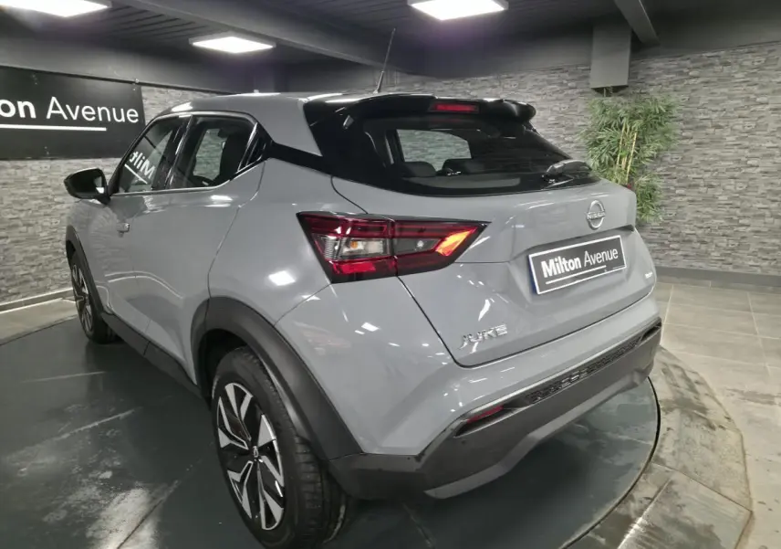 Vue 3/4 arrière droite d'un Nissan Juke gris métallisé 2023 avec jantes bi-ton et toit noir dans un showroom.