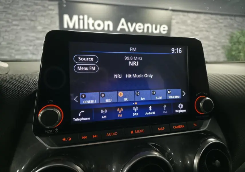 Écran tactile central du tableau de bord du Nissan Juke 2023 affichant la radio FM NRJ, avec commandes audio et climatisation visibles.