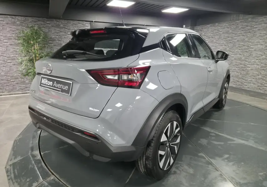 Vue 3/4 arrière droite du Nissan Juke 2023 gris métallisé avec jantes bi-ton et toit noir en intérieur showroom.