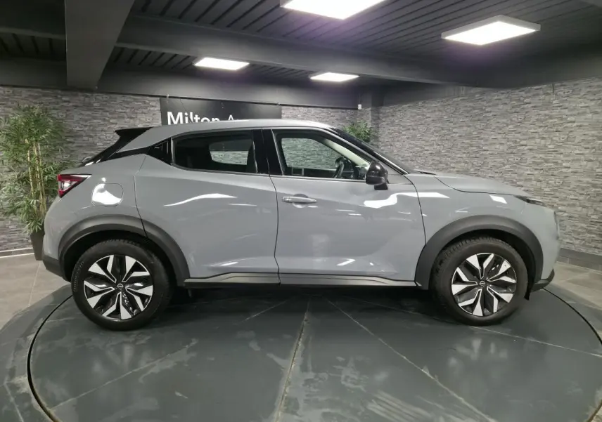 Profil droit d'un Nissan Juke gris métallisé 2023 avec jantes alliage bicolores et coques de rétroviseurs noires.