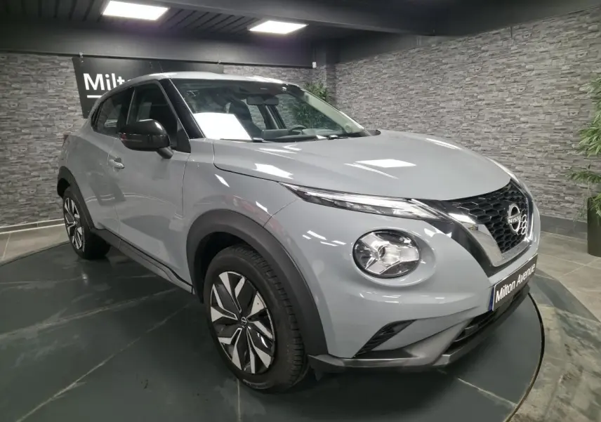 Nissan Juke gris métallisé vue 3/4 avant droit, avec jantes bi-ton et coques de rétroviseurs noires.