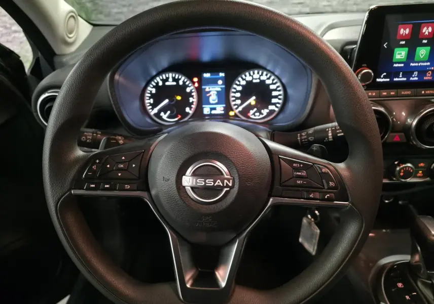 Vue rapprochée du volant noir de Nissan Juke 2023 avec tableau de bord et écran tactile en arrière-plan.