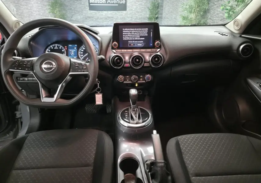 Vue intérieure avant du Nissan Juke gris 2023, tableau de bord avec écran tactile et volant multifonction.
