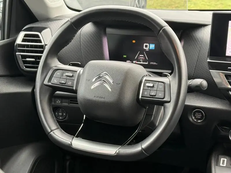 Vue rapprochée du volant cuir noir du Citroën C4 X 2024 avec commandes intégrées et tableau de bord numérique.
