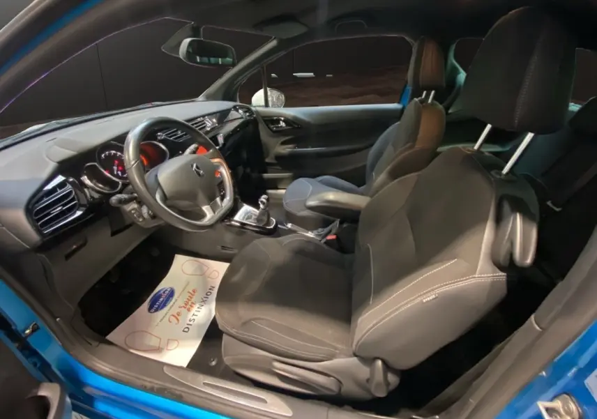 Vue intérieure côté conducteur de la Citroën DS3 e-HDi bleu, volant alu-cuir, sièges noirs et boîte manuelle visible.