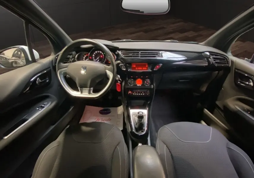 Vue intérieure avant de la Citroën DS3 e-HDi 90 Airdream So Chic 2011, tableau de bord noir brillant et volant alu-cuir.
