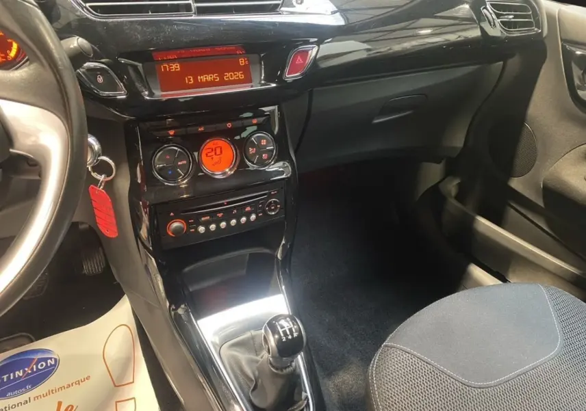 Vue intérieure centrée sur la console centrale et levier de vitesses manuelle d'une Citroën DS3 bleu, avec tableau de bord noir brillant.
