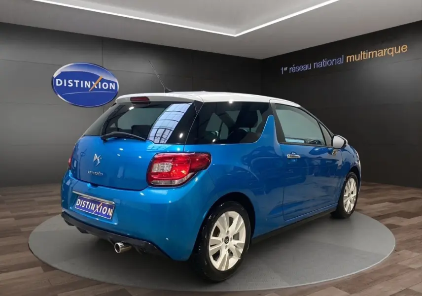 Vue 3/4 arrière droite d'une Citroën DS3 e-HDi 90 Airdream So Chic bleu avec toit blanc en showroom.