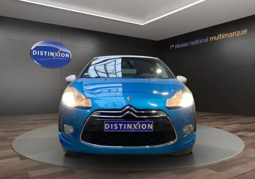 Vue avant d'une Citroën DS3 e-HDi 90 Airdream So Chic bleu avec phares allumés en showroom.