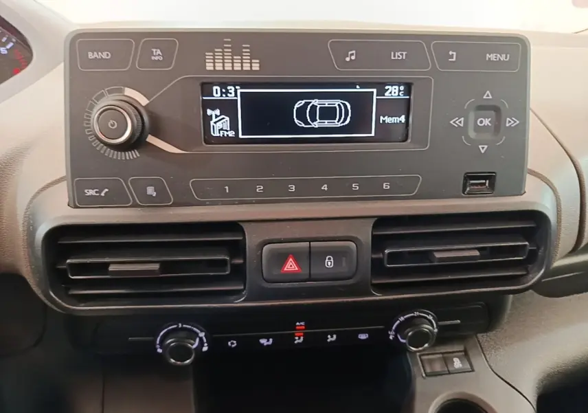 Vue rapprochée du tableau de bord du Peugeot Rifter avec écran multifonction et commandes de climatisation noires.