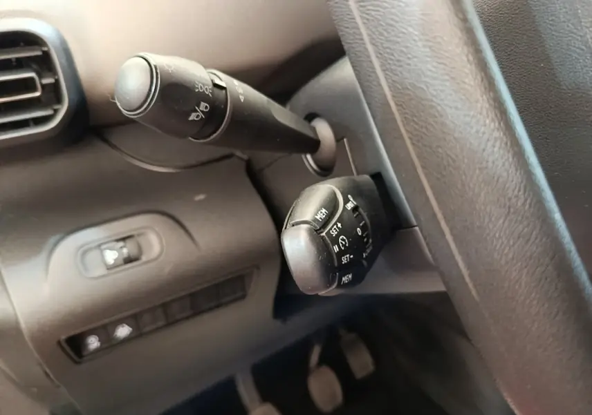 Gros plan sur les commandes au volant côté gauche du Peugeot Rifter blanc, avec boutons de régulateur de vitesse et éclairage.