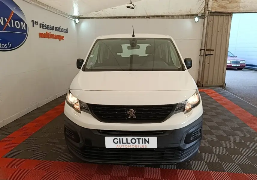 Vue avant d'un Peugeot Rifter blanc 2020 avec calandre noire et phares allumés dans un garage.