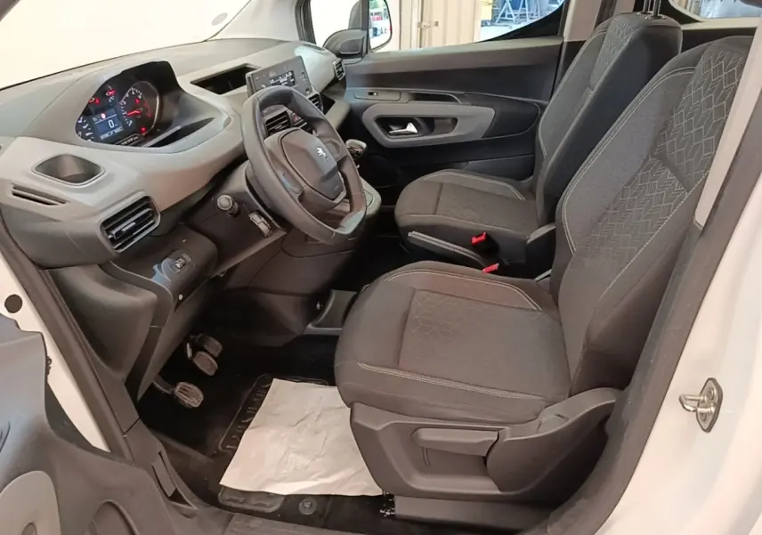 Vue intérieure côté conducteur du Peugeot Rifter blanc 2020, montrant sièges avant gris et tableau de bord avec volant.
