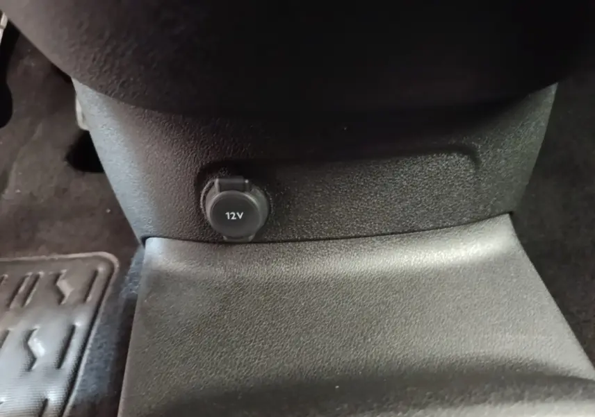Prise 12V noire en gros plan sur la console centrale intérieure du Peugeot Rifter blanc, vue rapprochée du bas.