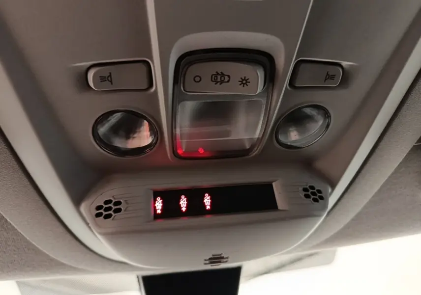 Vue en gros plan du plafonnier intérieur du Peugeot Rifter blanc, avec commandes d’éclairage et voyants de ceinture allumés.