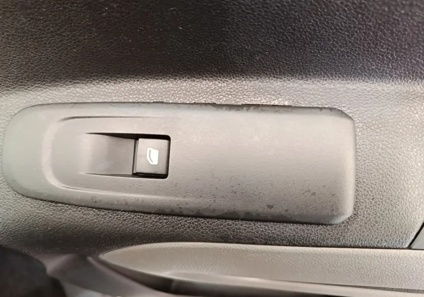 Gros plan sur l'interrupteur de lève-vitre électrique noir sur la porte intérieure d'un Peugeot Rifter blanc.