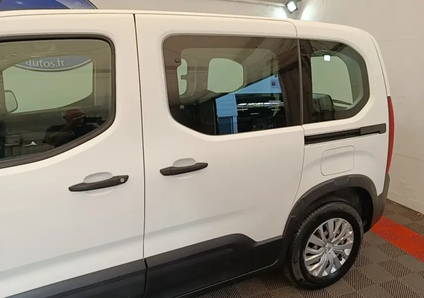 Vue latérale droite d'un Peugeot Rifter blanc, mettant en valeur les grandes fenêtres et les poignées de porte noires.