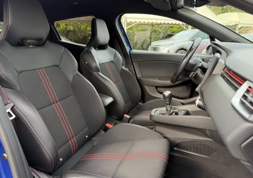 Vue intérieure côté conducteur de la Renault Clio RS Line bleu 2021, sièges sport noirs avec surpiqûres rouges.
