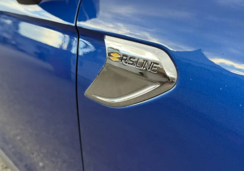 Gros plan sur l'emblème RS Line chromé sur la portière côté gauche d'une Renault Clio bleue.