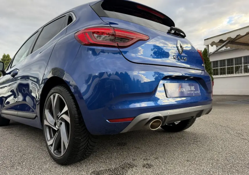 Vue 3/4 arrière droite d'une Renault Clio RS Line bleu, avec échappement chromé et jantes alliage distinctives.