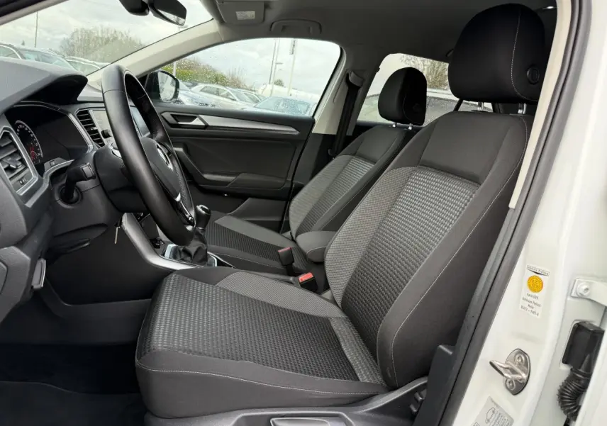 Vue intérieure côté conducteur du Volkswagen T-Roc blanc pur 2021, sièges avant en tissu gris et volant cuir multifonction.