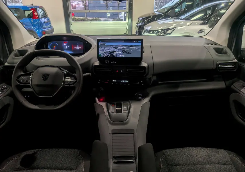 Vue intérieure frontale du Peugeot Rifter gris acier 2025, mettant en valeur le tableau de bord numérique et l'écran tactile central.
