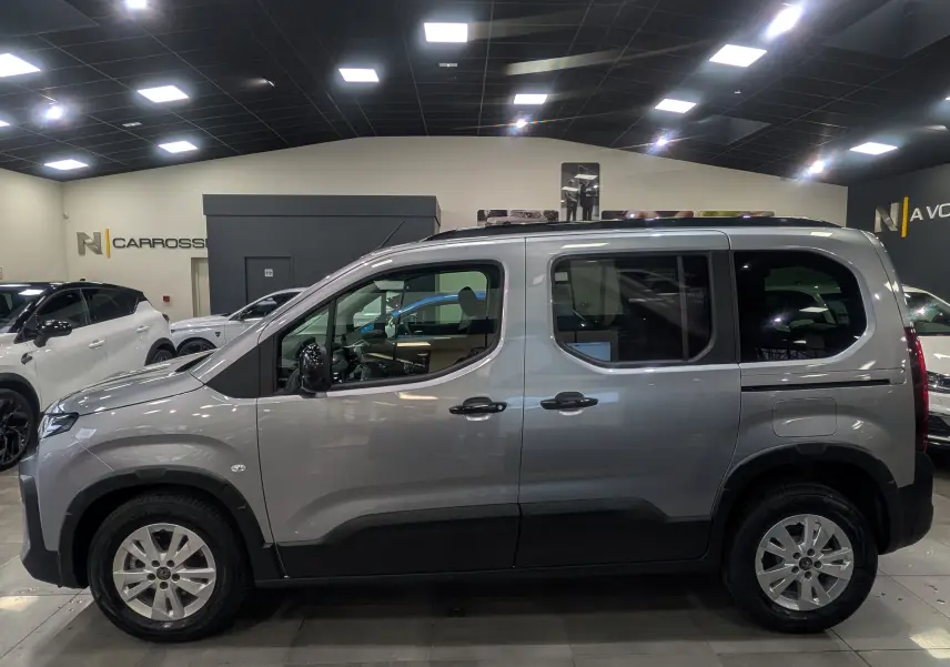 Vue de profil côté gauche d’un Peugeot Rifter gris acier 2025 en intérieur, avec jantes alliage et vitres teintées.