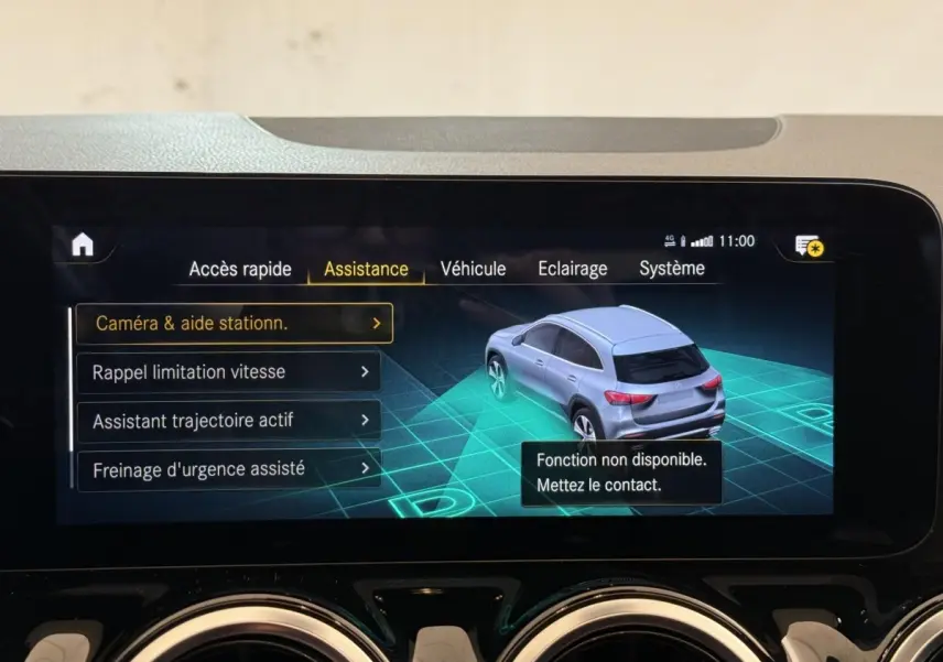 Écran tactile intérieur affichant l'assistance au stationnement avec vue 3D d'un Mercedes GLA gris clair en 3/4 arrière.