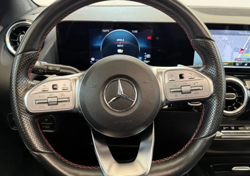 Vue rapprochée du volant cuir noir avec surpiqûres rouges et tableau de bord numérique du Mercedes GLA 250 e AMG Line 2023.