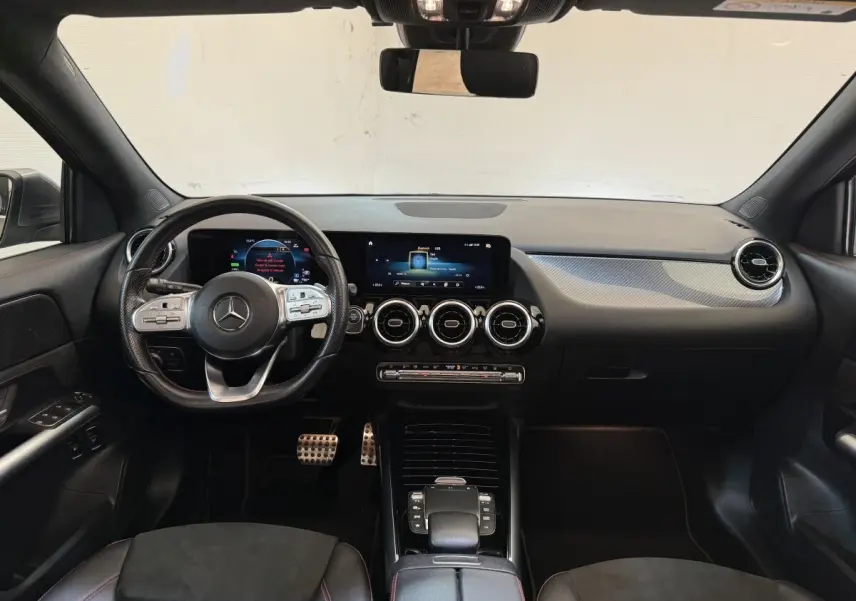 Vue intérieure avant du tableau de bord noir de la Mercedes GLA 250 e AMG Line avec volant cuir multifonctions et écran tactile.