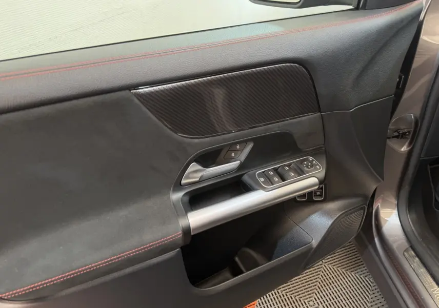 Vue rapprochée de la porte avant gauche gris clair du Mercedes GLA 250 e AMG Line avec garniture noire et surpiqûres rouges.