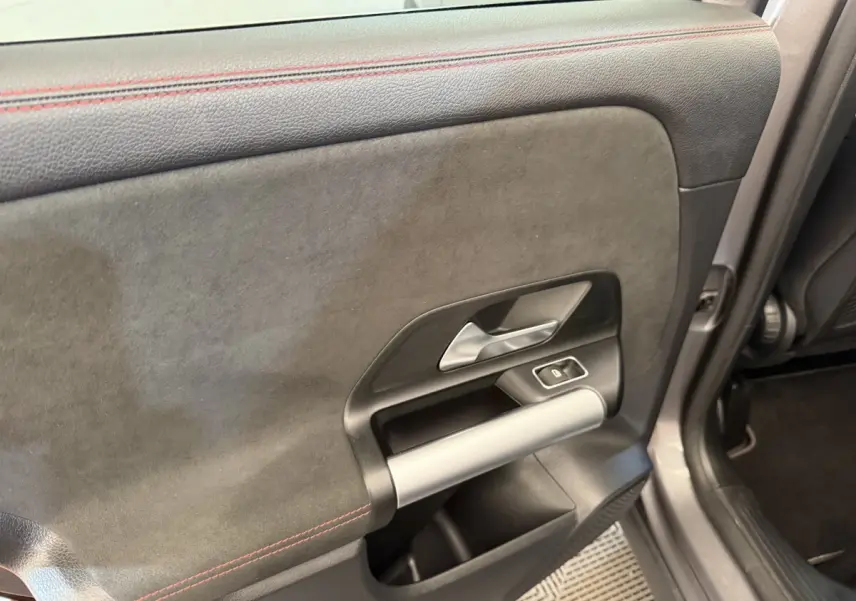Gros plan sur la porte intérieure côté gauche du Mercedes GLA 250 e AMG Line gris clair, avec surpiqûres rouges et poignée argentée.