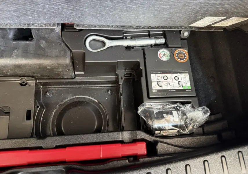 Vue rapprochée du compartiment de rangement sous le coffre du Mercedes GLA 250 e AMG Line gris clair, montrant outils et compresseur.