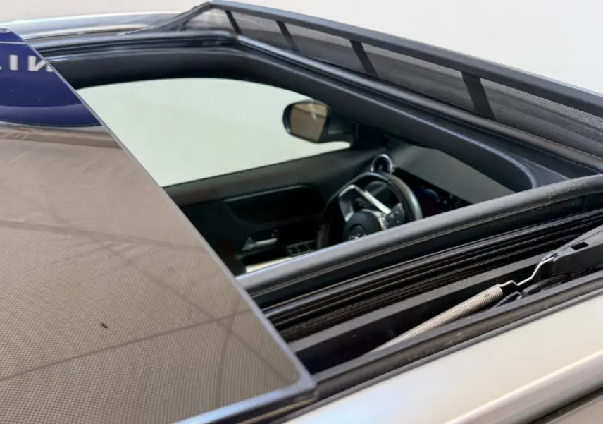 Vue rapprochée du toit ouvrant ouvert et intérieur côté conducteur d’une Mercedes GLA 250 e AMG Line gris clair.
