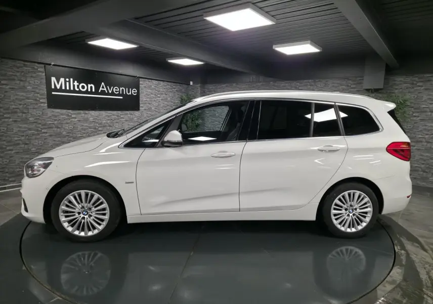 BMW Série 2 Gran Tourer blanc vue de profil gauche, jantes alliage 17'' et vitres teintées dans un showroom.