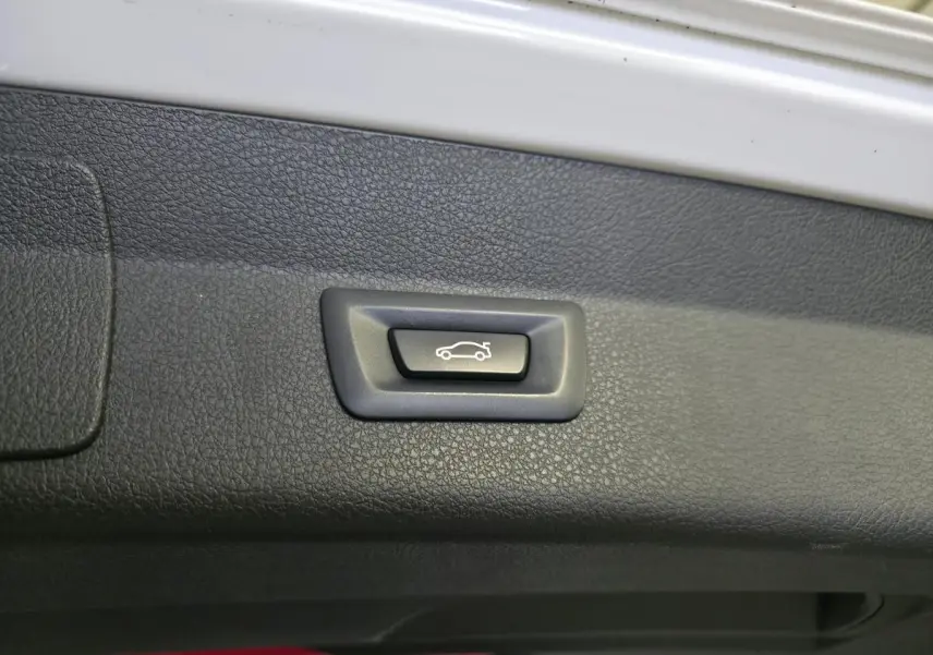 Bouton d'ouverture électrique du hayon sur la garniture intérieure noire d'une BMW Série 2 Gran Tourer blanche.