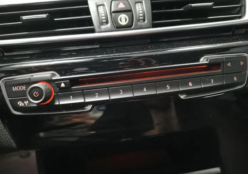 Gros plan sur la commande radio BMW noire avec boutons numérotés et éclairage rouge à l'intérieur du véhicule.
