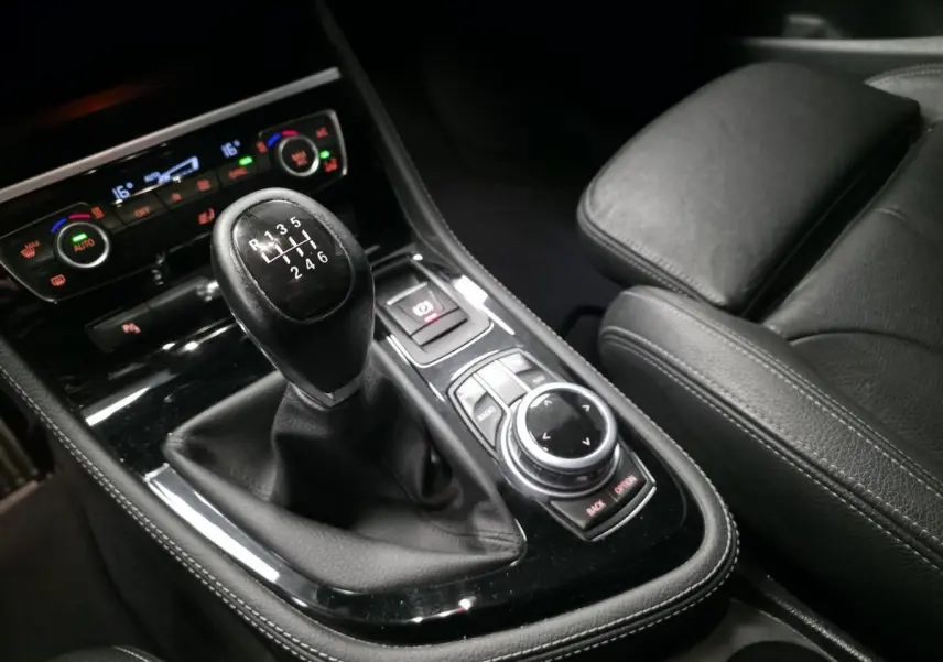 Gros plan sur la console centrale intérieure noire d'une BMW Série 2 218d xDrive avec levier de vitesse manuel et commandes iDrive.