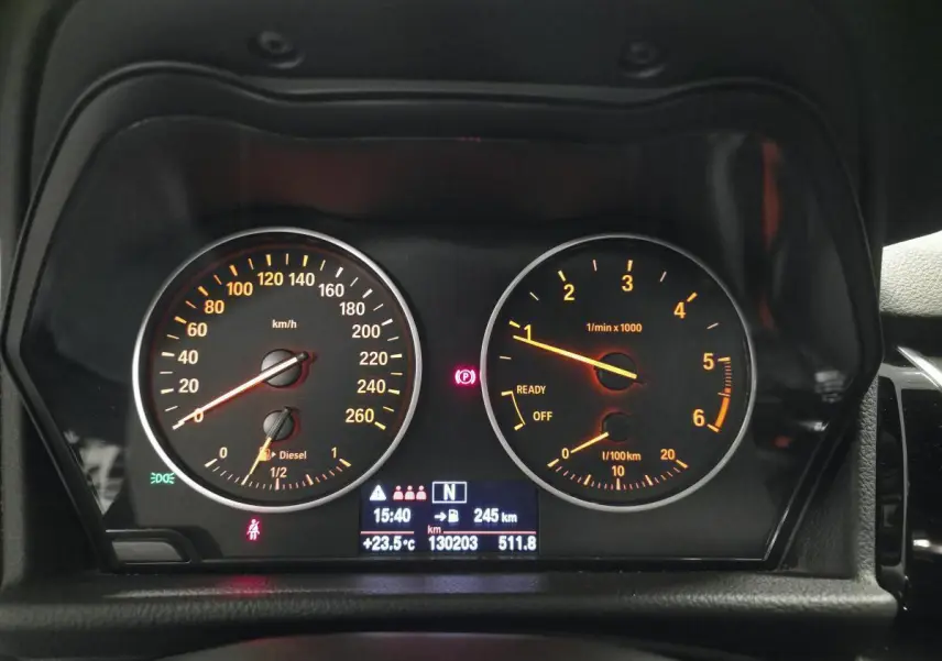 Vue rapprochée du tableau de bord noir d'une BMW Série 2 218d xDrive avec compteurs analogiques orange et écran digital central.