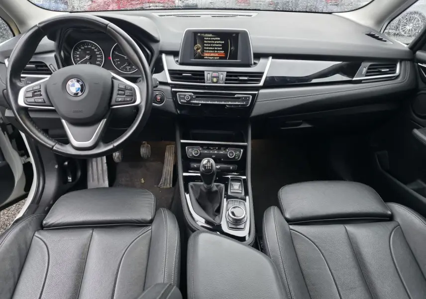 Vue intérieure avant de la BMW Série 2 Gran Tourer 218d xDrive 2016, volant cuir, console centrale avec boîte manuelle.