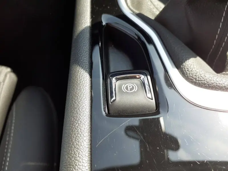 Détail du bouton de frein à main électrique sur la console centrale noire brillante d’une Opel Insignia Grand Sport gris clair.