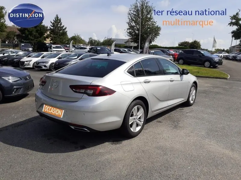 Opel Insignia Grand Sport gris clair vue 3/4 arrière droit sur parking avec plaque "OCCASION" visible.
