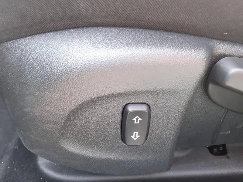 Bouton de réglage de siège en plastique noir sur le côté intérieur d’un Opel Insignia Grand Sport gris clair.