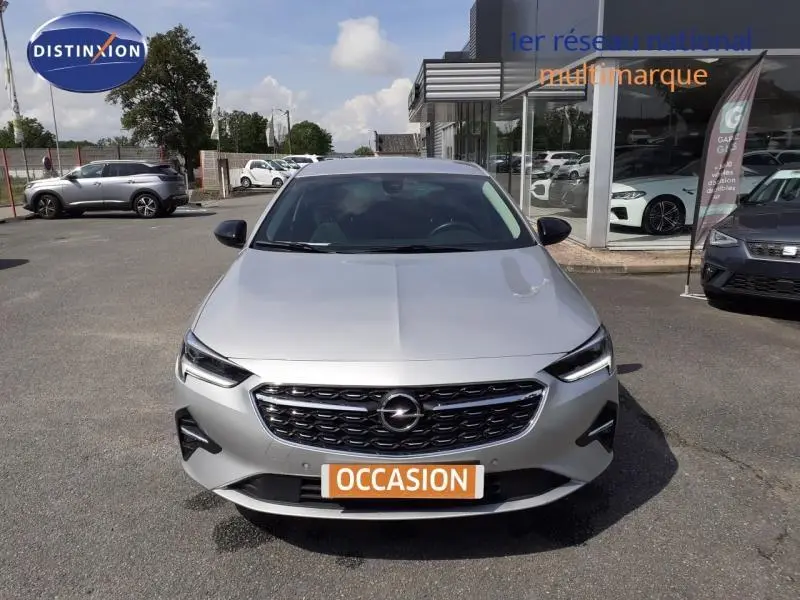 Vue avant d'une Opel Insignia Grand Sport gris clair 2021 avec calandre noire et plaque "OCCASION" en orange.