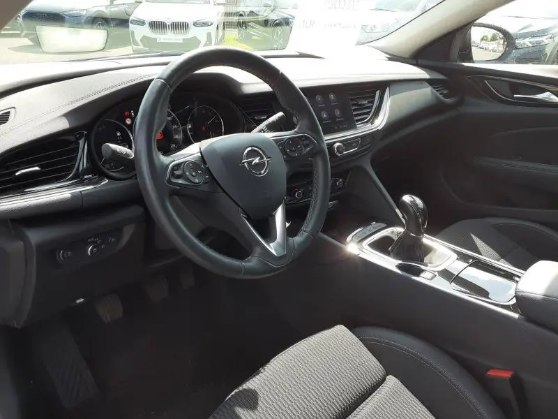 Vue intérieure côté conducteur de l'Opel Insignia Grand Sport 2021, tableau de bord noir avec volant multifonction et levier de vitesse.