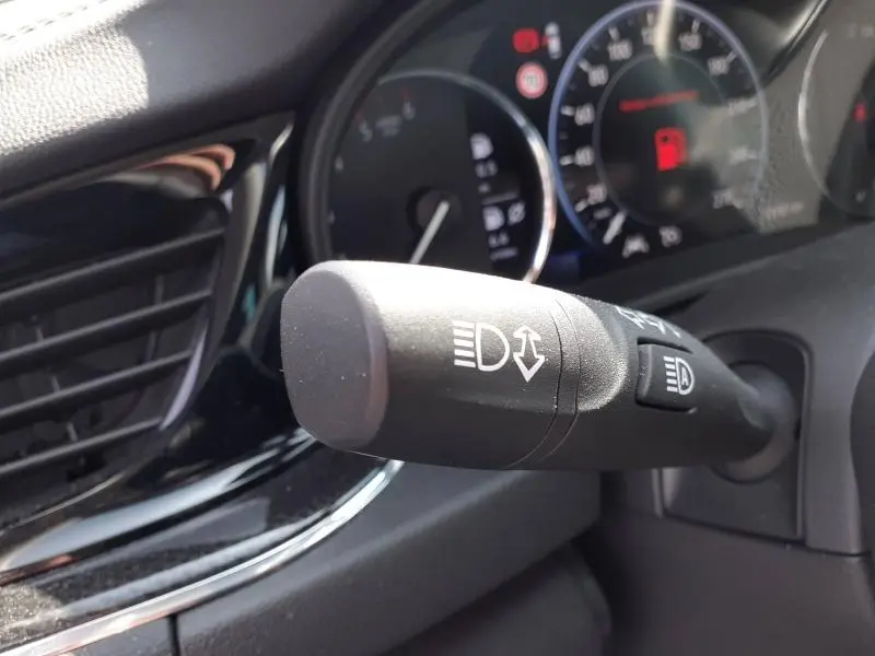 Gros plan sur la commande des phares à gauche du volant dans l’habitacle de l’Opel Insignia Grand Sport gris clair 2021.