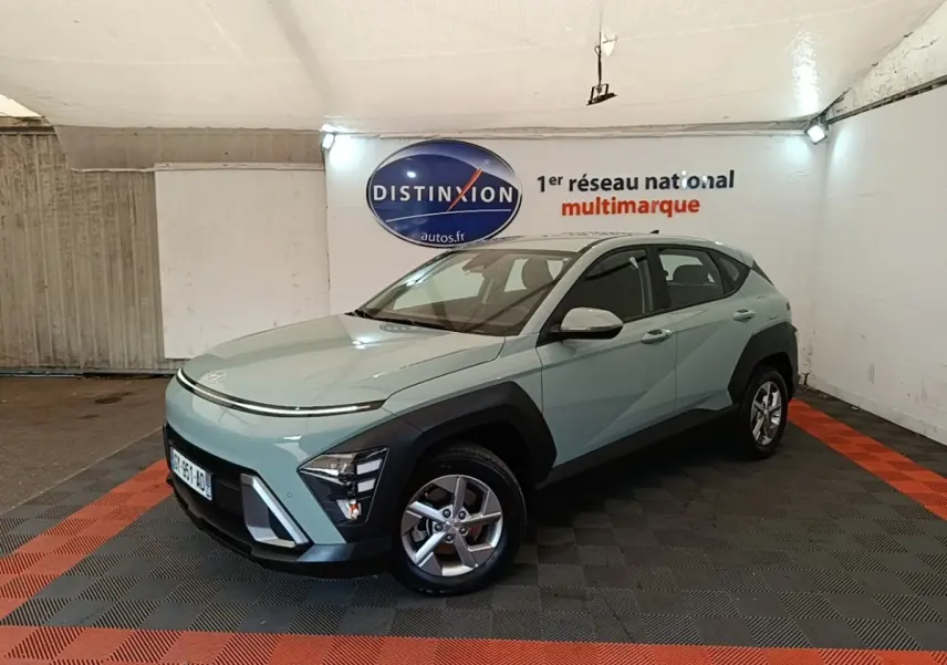 Vue 3/4 avant droite d’un Hyundai Kona 2024 vert clair avec protections noires et jantes alliage en intérieur showroom.