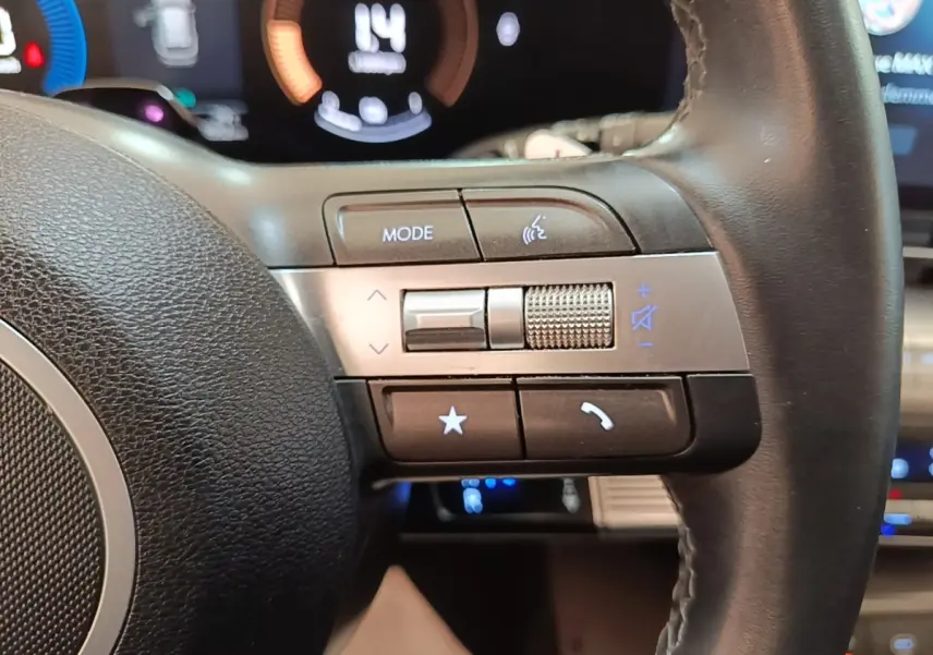 Gros plan sur les commandes multifonctions en cuir du volant du Hyundai Kona 1.6 Hybrid 2024, avec affichage numérique en arrière-plan.