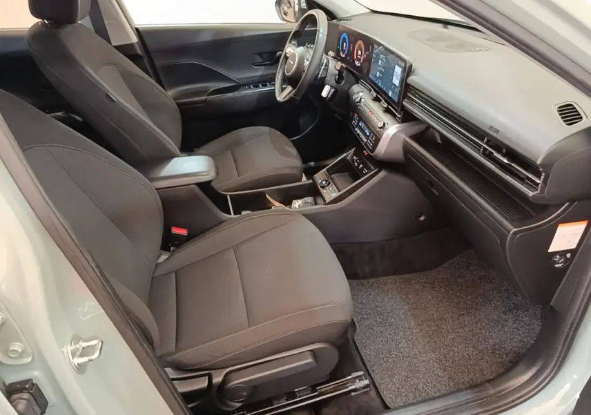 Vue intérieure côté conducteur de la Hyundai KONA 2024, sièges noirs et tableau de bord avec écran tactile large.